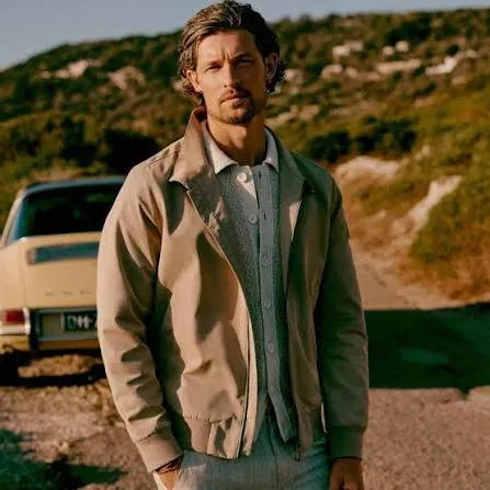 Man in beige jas bij een klassieke auto in een mediterraan landschap