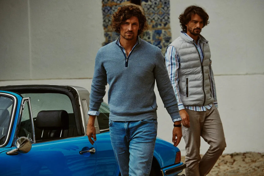 Man in blauwe trui met halve rits naast een blauwe klassieke auto